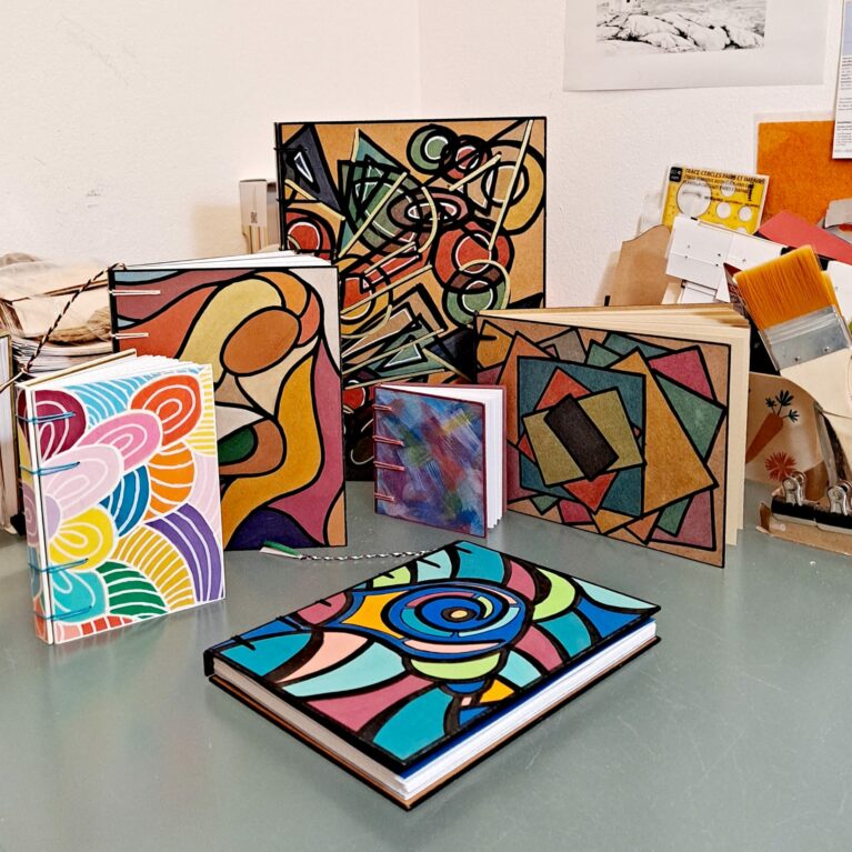 Mes p'tits carnets - Création France. Plusieurs carnets sont disposés sur une table de travail.