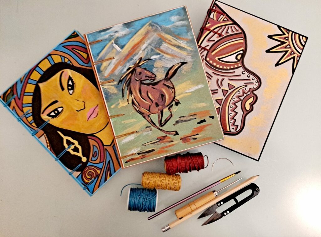 Trois p'tits carnets ainsi que du fil de reliure et des outils sont exposés sur une table