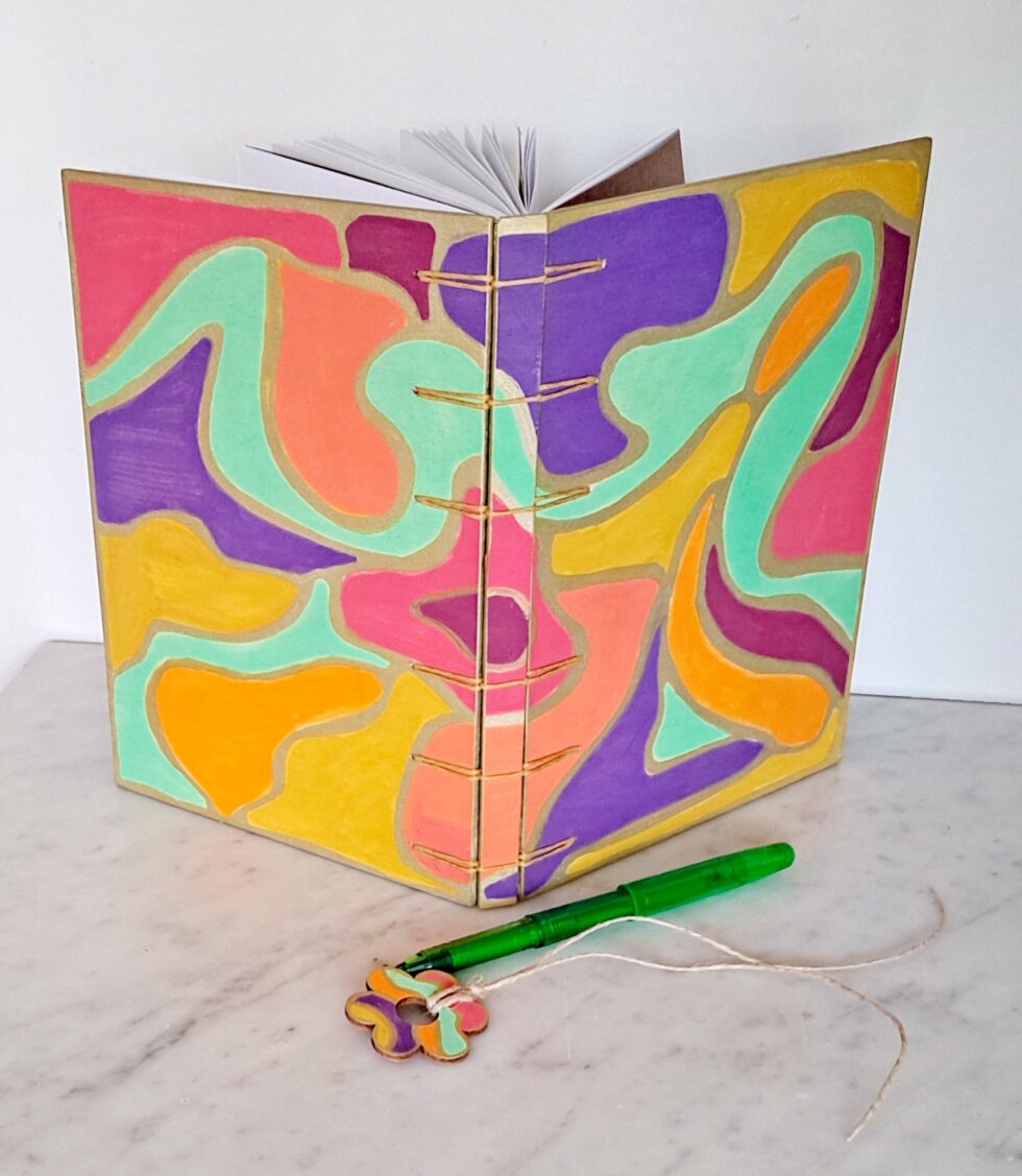 Carnet NÄSS face ouvert debout avec stylo vert et marque page fleur en bois.