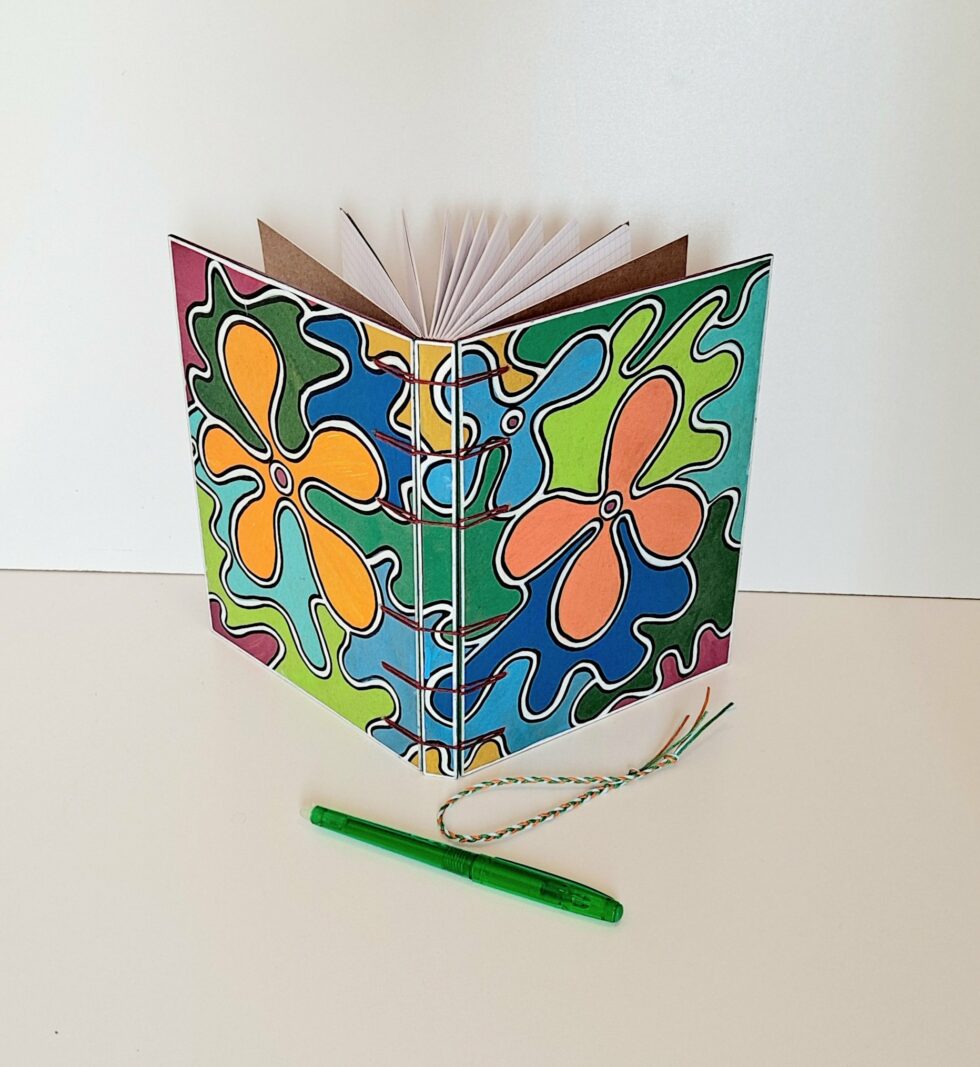 Carnet CAPUCINE, vue recto verso debout avec stylo vert et marque page fleur.