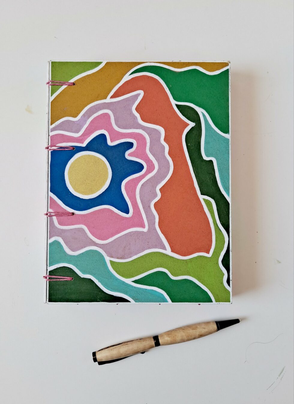 Boîte à mots CHARLIE vue recto à plat sur reliure rose avec carnets et stylo en bois.