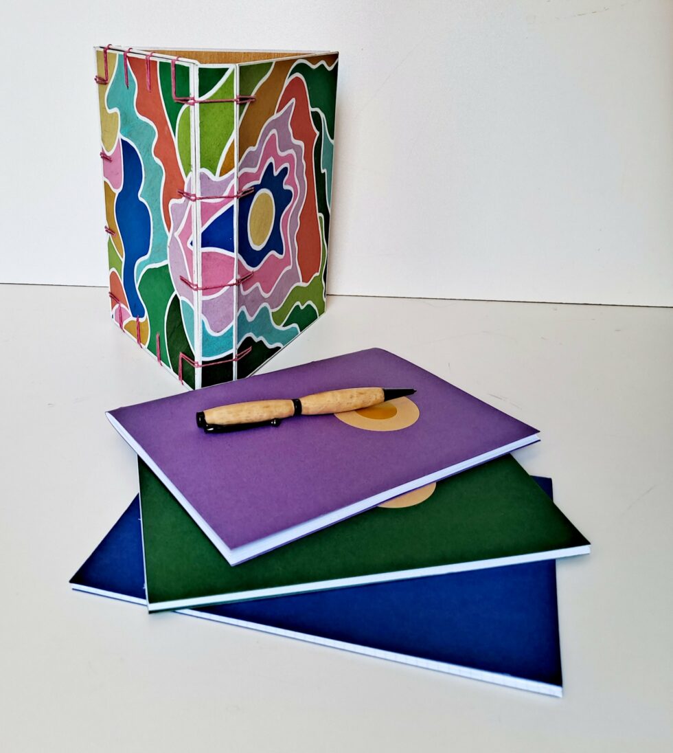 Boîte à mots CHARLIE vue debout sur dos avec carnets et stylo en bois.