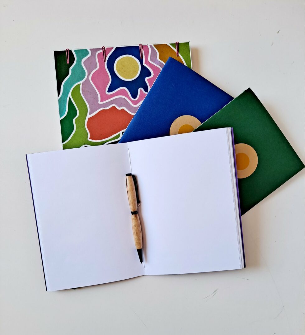 Boîte à mots CHARLIE vue sur pages sur dos reliure rose avec carnets et stylo en bois.