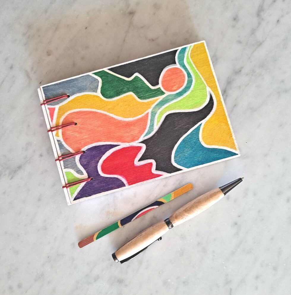 Carnet EMPREINTES vue recto à plat avec reliure rouge avec marque pages et stylo en bois.