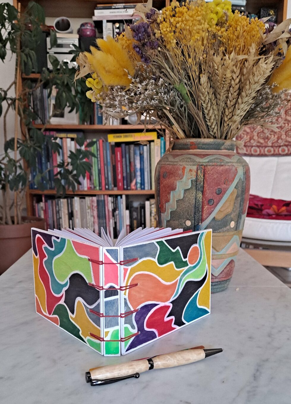 Carnet EMPREINTES vue recto verso debout avec dos et reliure rouge avec marque pages et stylo en bois.