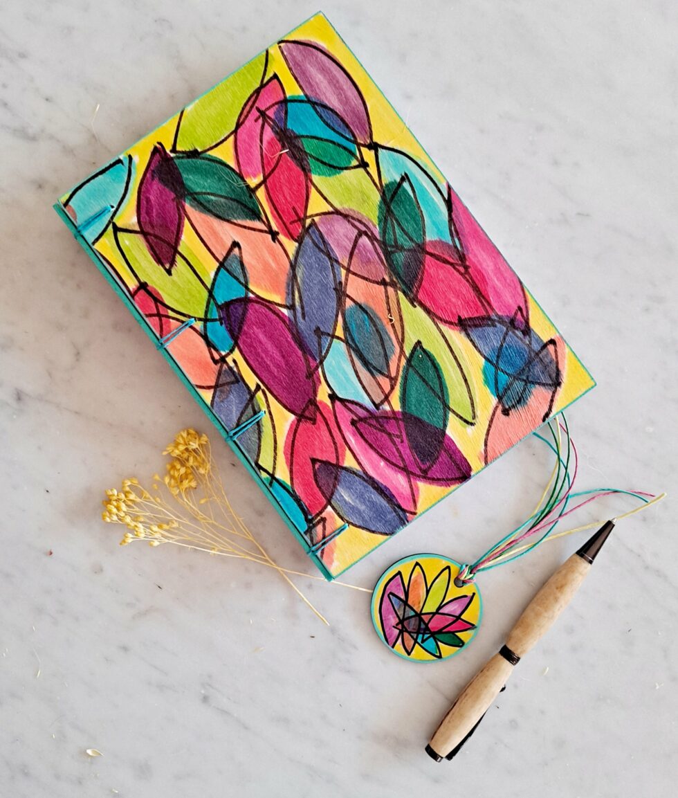 Carnet JELLY vue recto à plat avec dos fil turquoise et fleur jaune et marque-pages en bois et stylo en bois.
