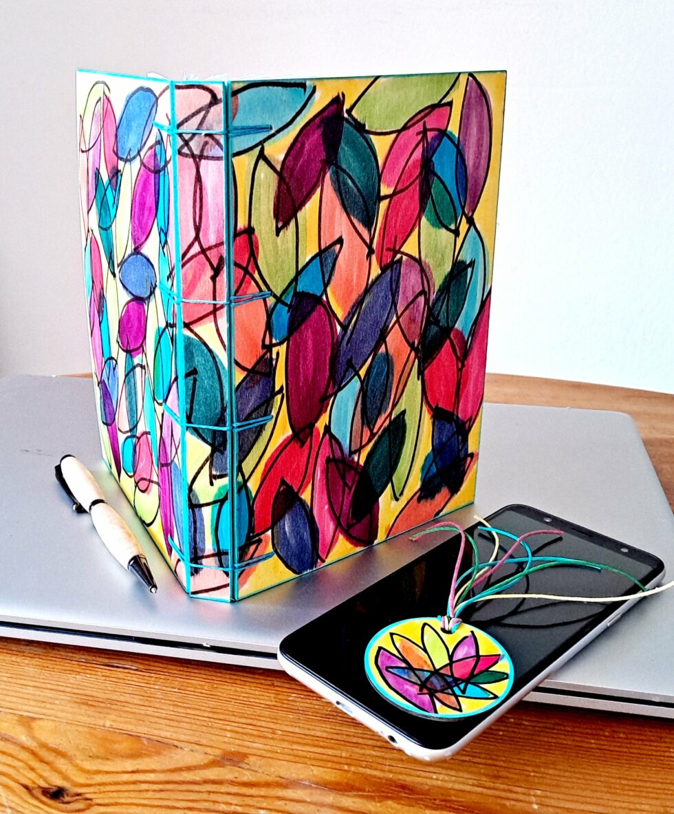 Carnet JELLY vue recto verso debout avec stylo en bois, marque-pages en bois téléphone et ordinateur.