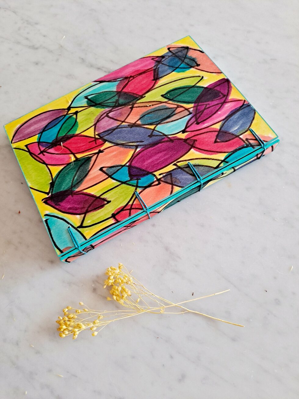 Carnet JELLY vue recto à plat avec dos fil turquoise et fleur jaune.