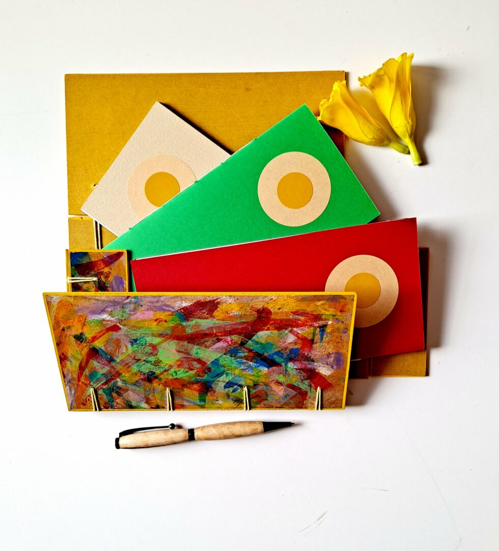 Boîte à mots OASIS vue recto côté droit ouvert sur reliure jaune avec stylo en bois et 2 fleurs jaunes.