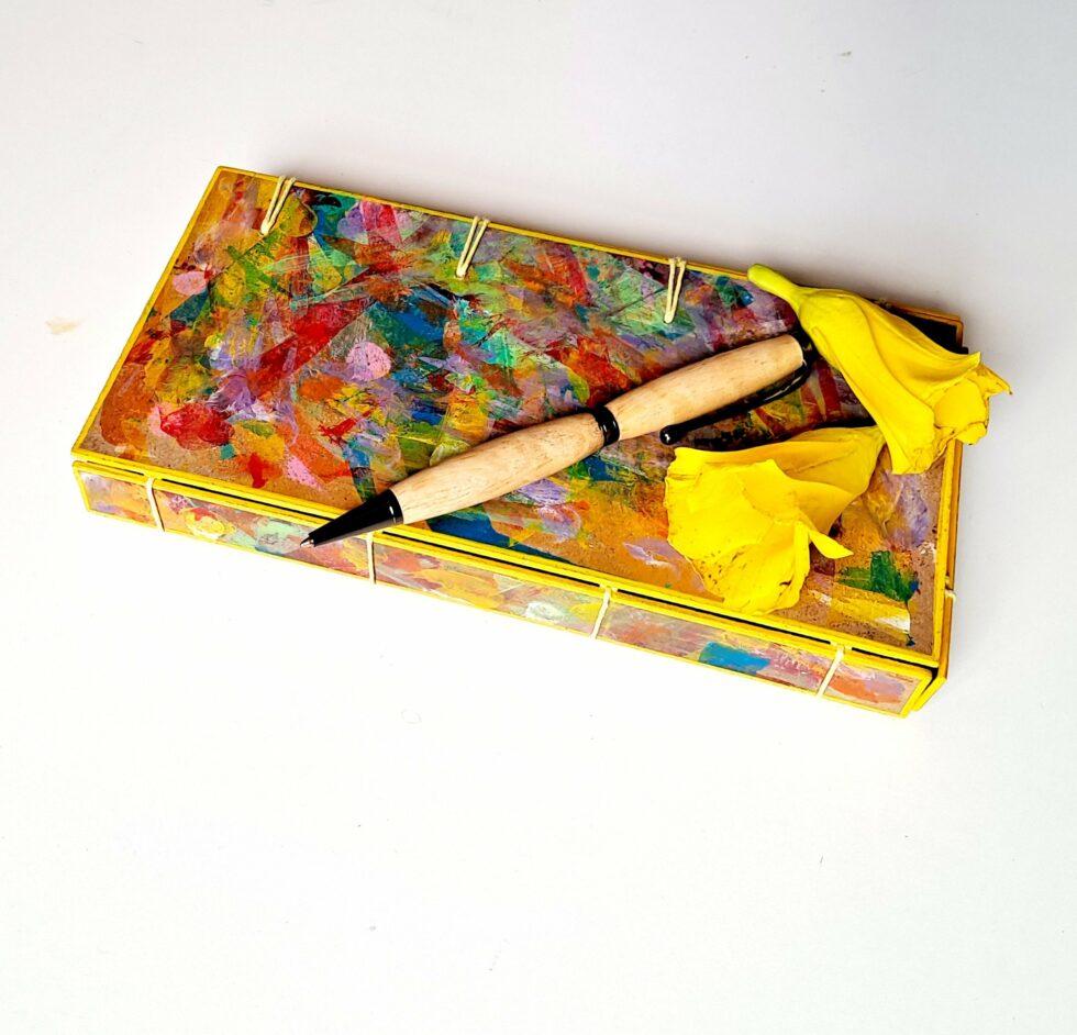 Boîte à mots OASIS vue recto fermée avec stylo en bois et 2 fleurs jaunes.