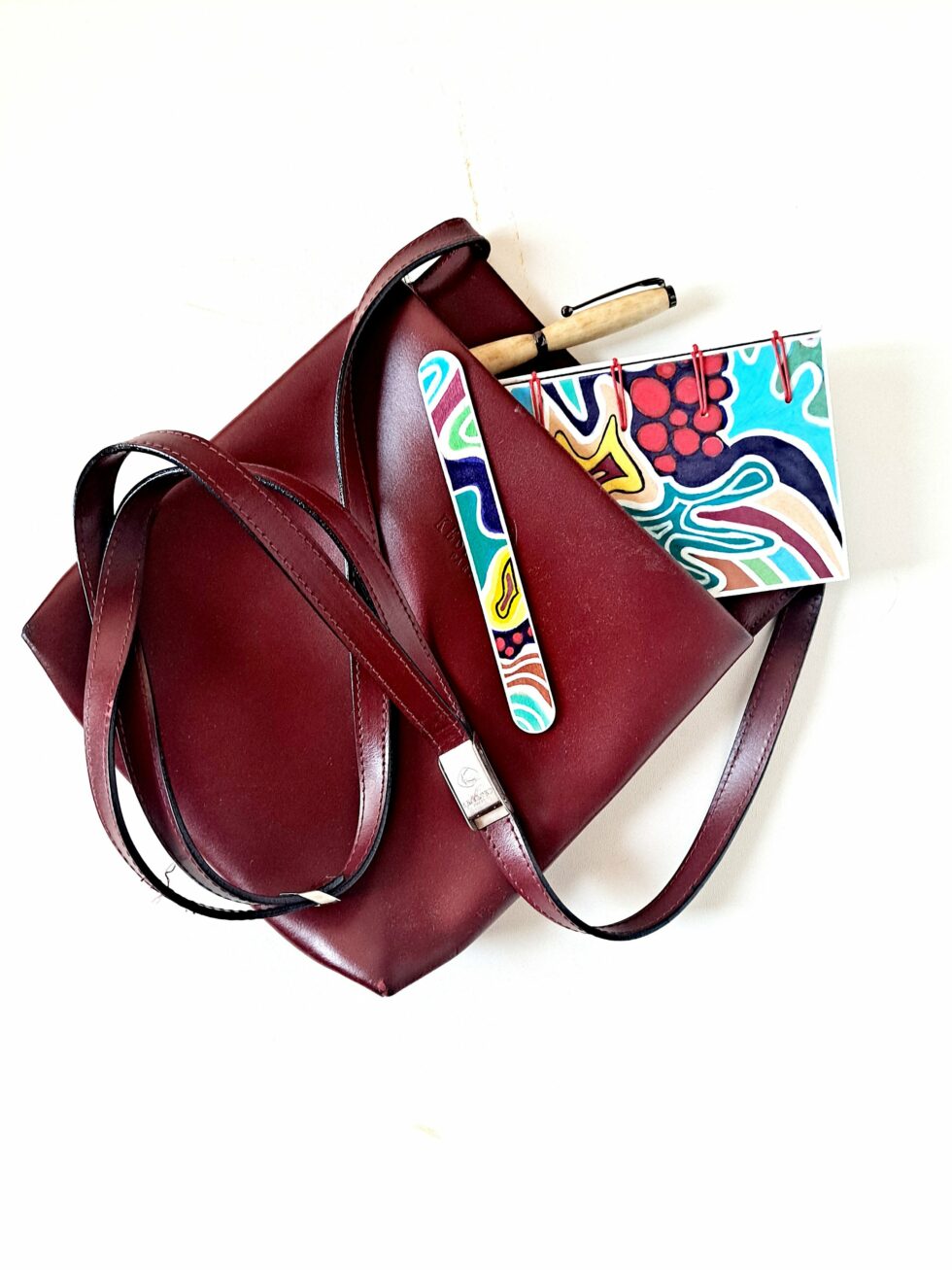 Carnet ATOCA vue recto dans sac rouge avec stylo en bois et marque pages en bois peint.