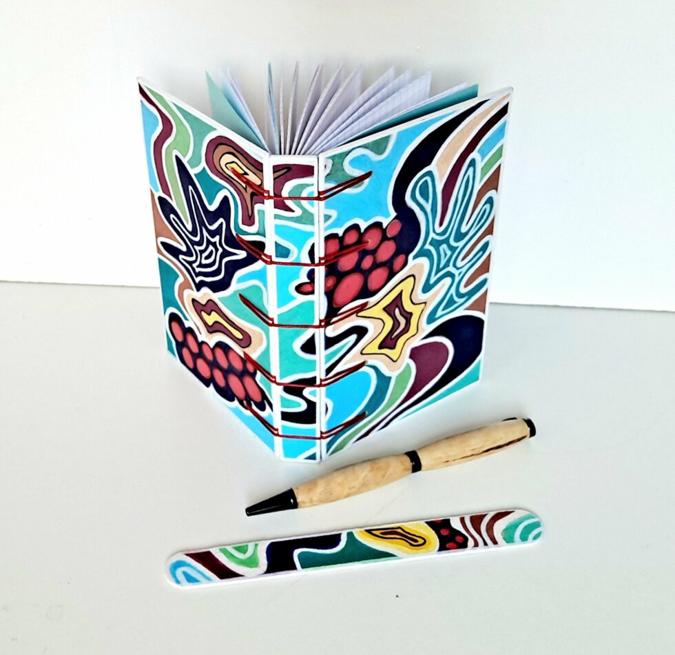 Carnet ATOCA vue recto verso debout avec stylo en bois et marque pages en bois peint.