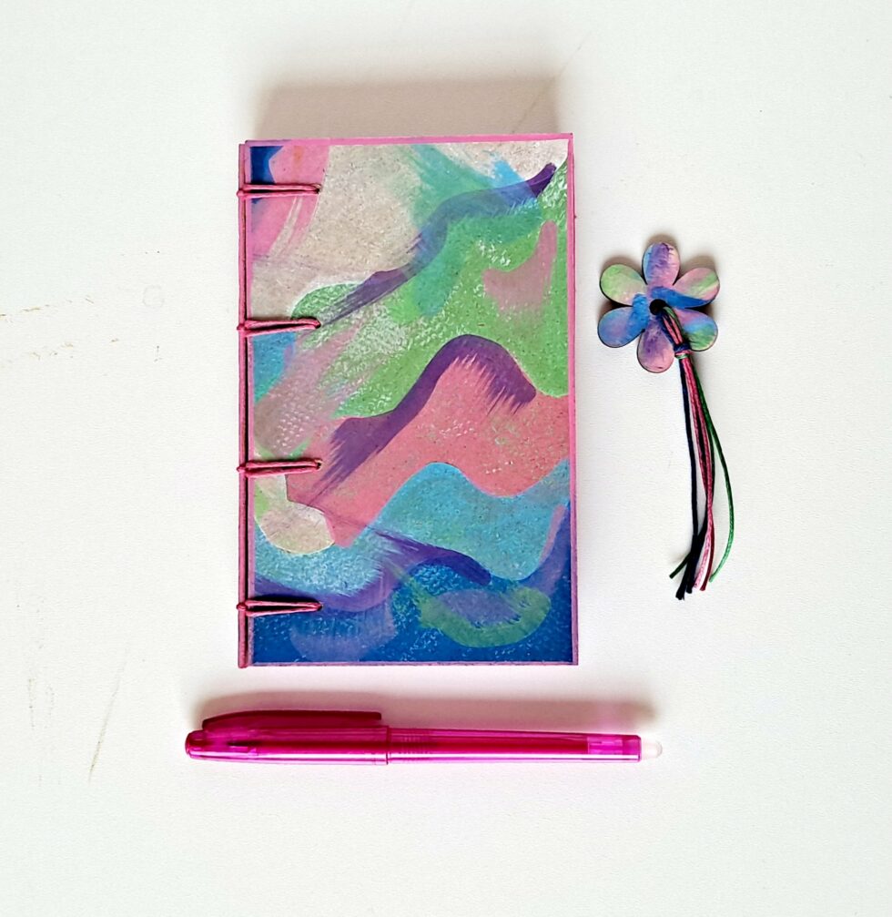 Carnet PASTEL vue recto à plat reliure rose avec marque pages en bois peint et stylo rose.