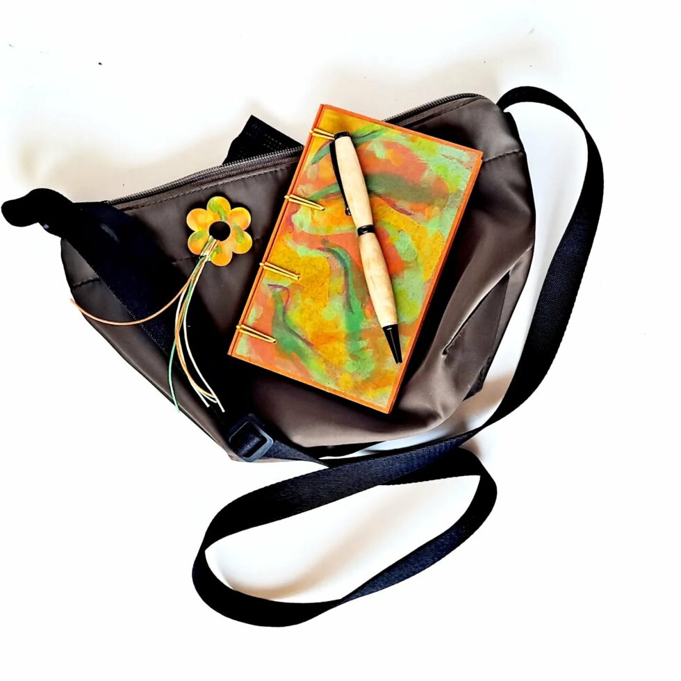Carnet VENCE vue recto sur sac avec son marque-pages fleur bois peint et stylo en bois.