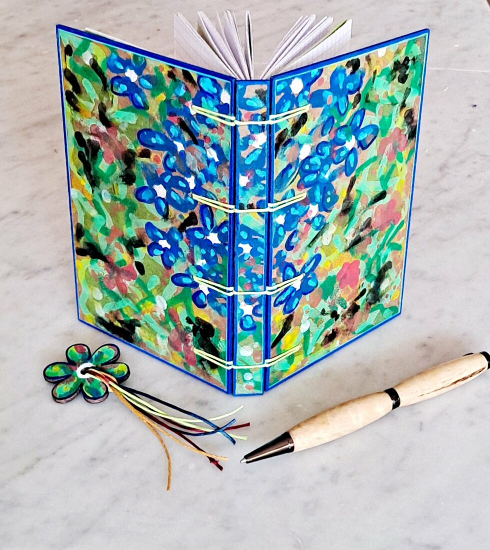 Carnet GENTIANE vue couverture fleurs recto verso debout avec reliure fil jaune et marque-pages fleur et stylo en bois.