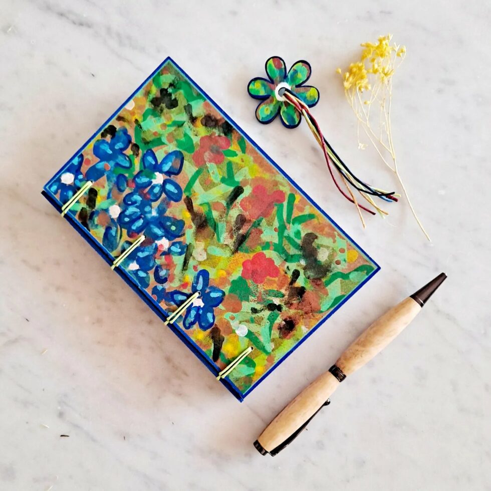 Carnet GENTIANE vue recto à plat avec marque-pages fleur et stylo en bois et fleur séchée jaune.