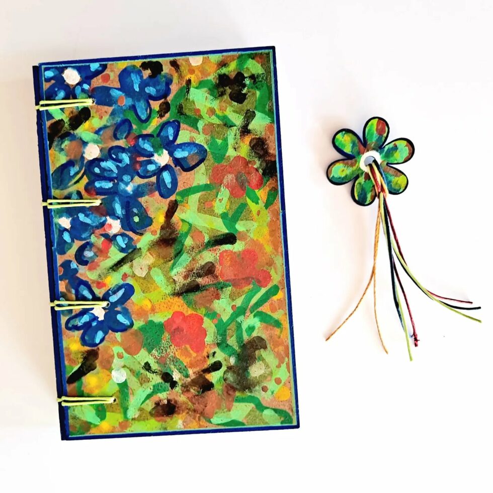 Carnet GENTIANE vue recto à plat avec reliure fil jaune et marque-pages fleur et stylo en bois et fleur séchée jaune.