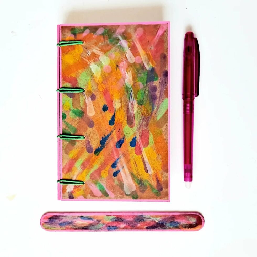 Carnet MONA, vue recto à plat avec marque-pages en bois et stylo rose.