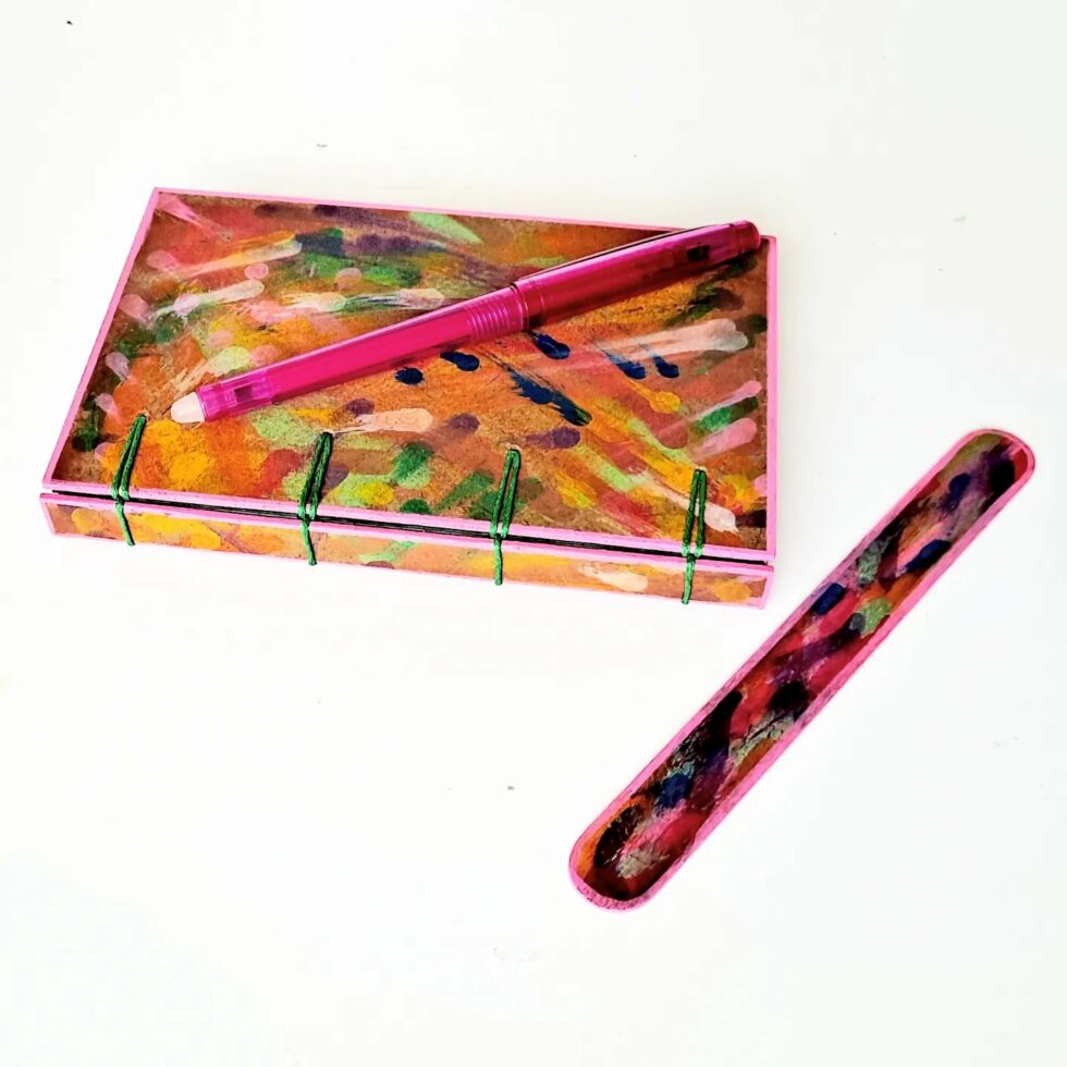 Carnet MONA, vue recto à plat avec dos avec marque-pages en bois et stylo rose.