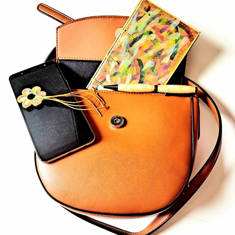 Carnet FIDJI vue recto dans sac avec marque-pages fleur et stylo en bois.
