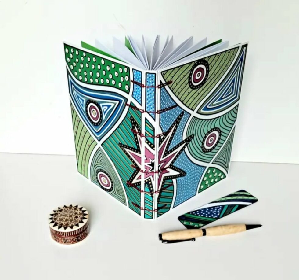 Carnet DJINJA, vue recto verso debout avec stylo en bois et reliure rouge.