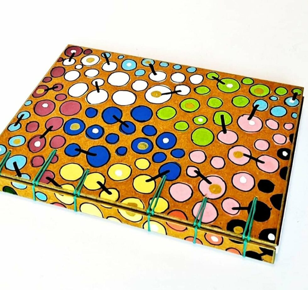 Carnet FARRAGO, vue recto avec dos avec reliure turquoise et stylo multicolore.