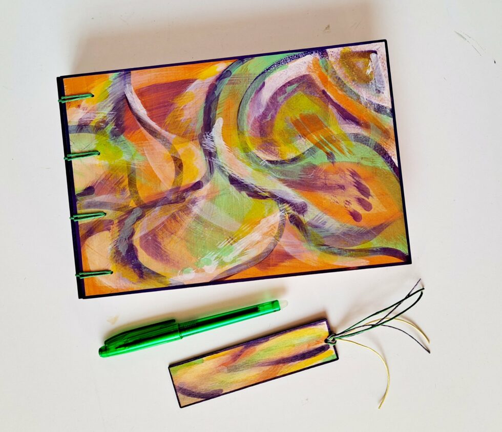 Album MAHÉ, vue recto à plat avec marque-pages en bois peint et stylo vert.