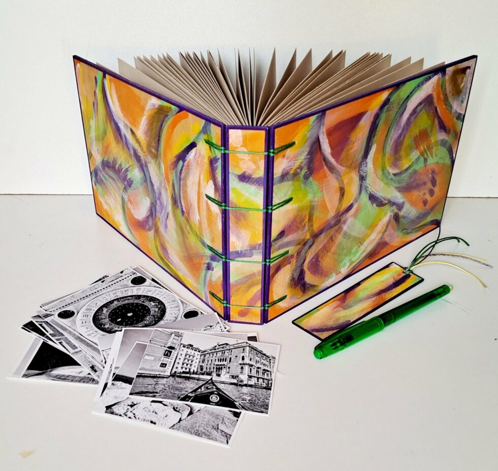 Album MAHÉ, vue recto verso debout avec marque-pages en bois peint et stylo vert.