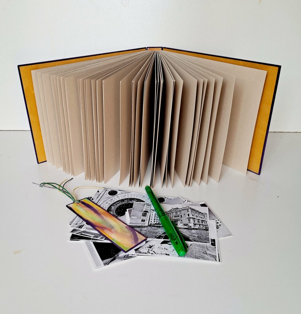 Album MAHÉ, vue intérieure debout sur pages et couverture avec marque-pages en bois peint et stylo vert.
