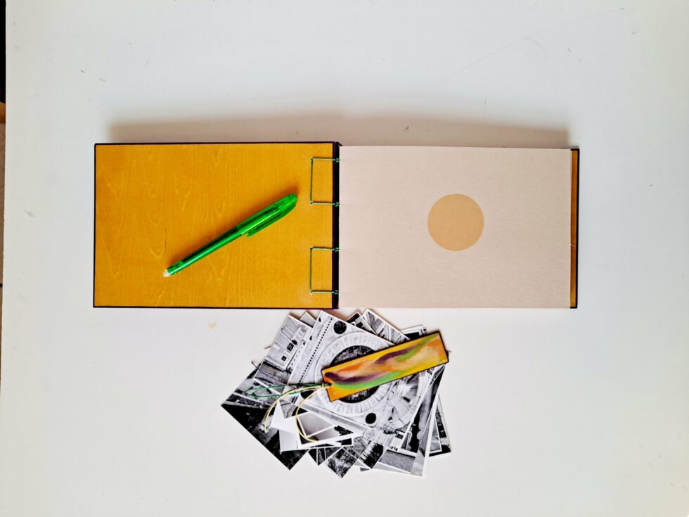 Album MAHÉ, vue intérieure sur pages et couverture avec marque-pages en bois peint et stylo vert.