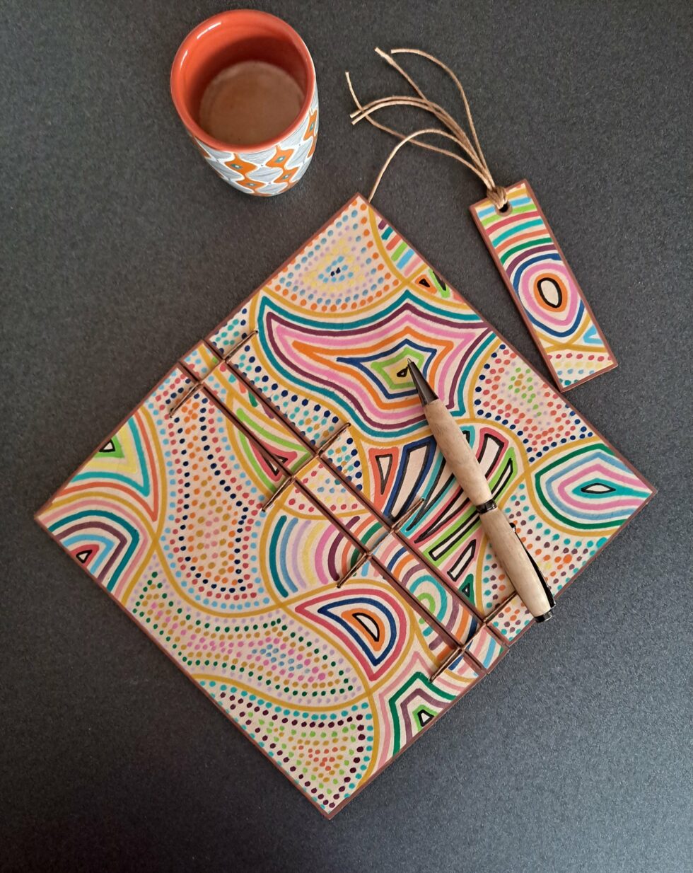Carnet KIMBA, vue recto verso avec marque-pages en bois peint à la main et stylo et tasse à café.