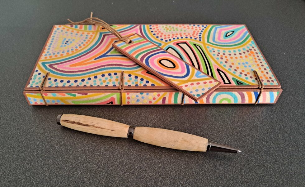 Carnet KIMBA, vue recto sur dos avec marque-pages en bois peint à la main et stylo en bois peint.