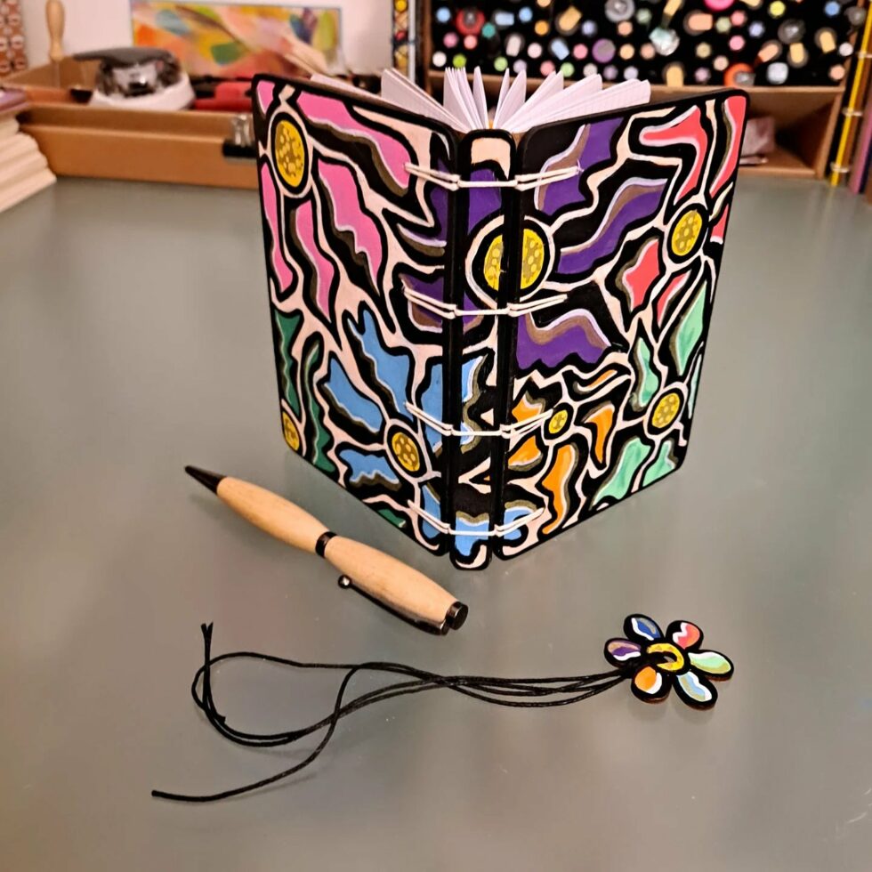 Carnet FLEUR, vue recto verso debout avec couverture en bois peint avec marque-pages en bois peint et stylo.