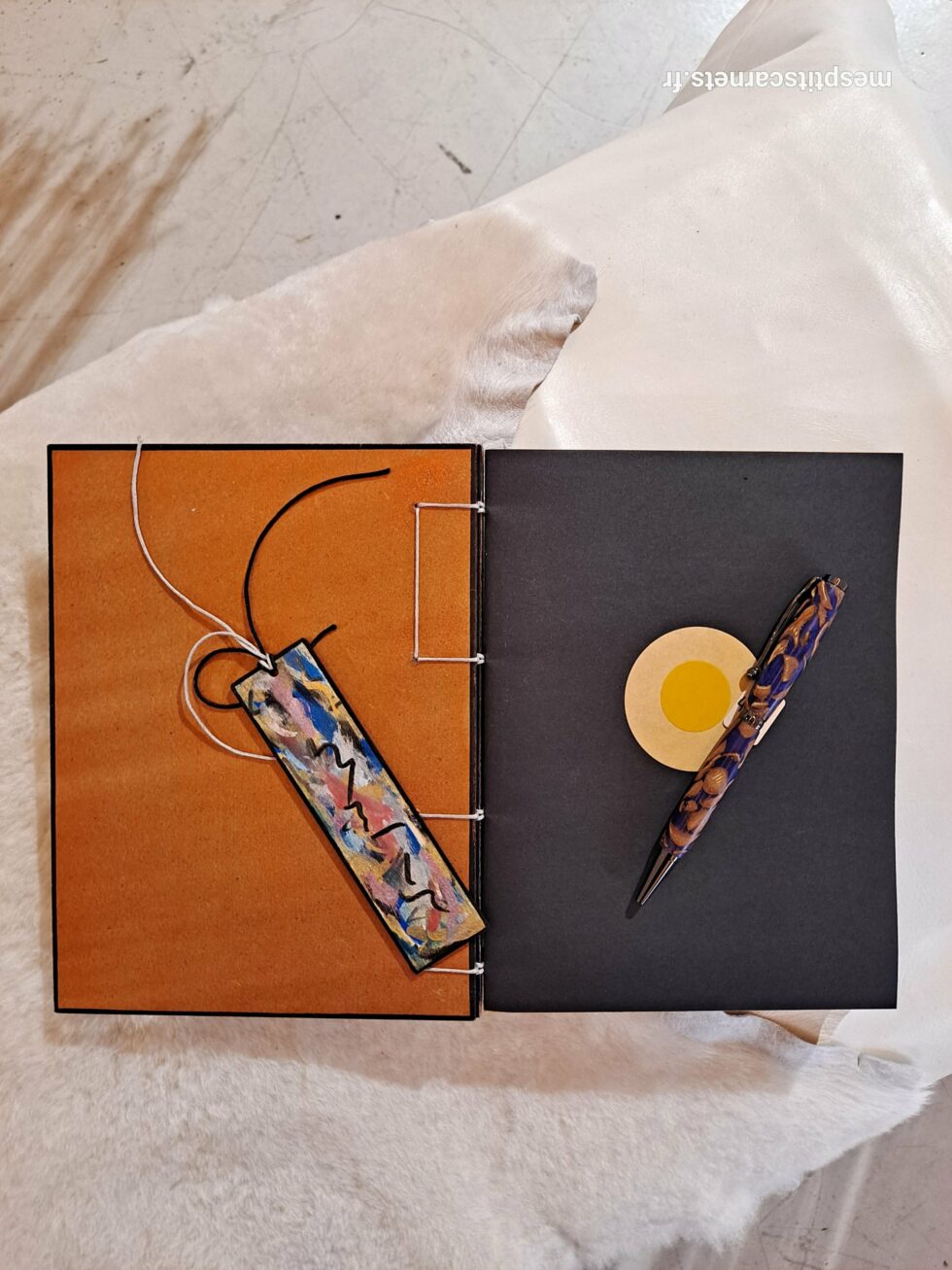 Carnet FRAC, vue intérieure sur pages avec marque-pages en bois peint et stylo.