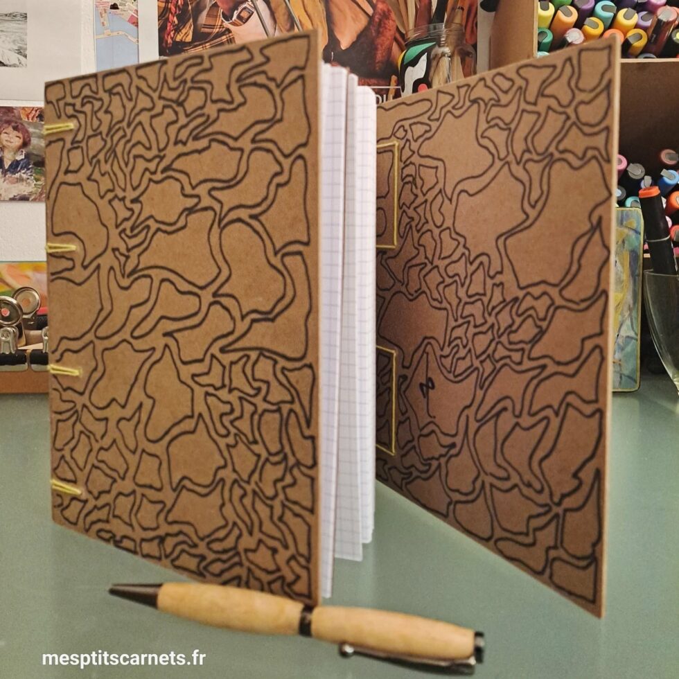 Carnet Triptyque OUED vue ouvert debout et couverture en bois peint et stylo.