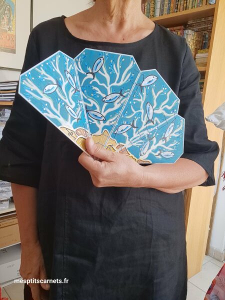 Eventail CORAIL en bois peint à la main, vue face ouvert en démonstration à la main, en mouvement, pour le format.